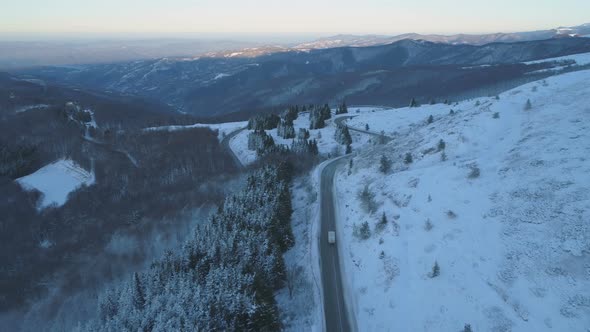 Drone Follows Big Rig Semi Truck Driving on Winding Winter Snow Road with Snowy Forest. alt