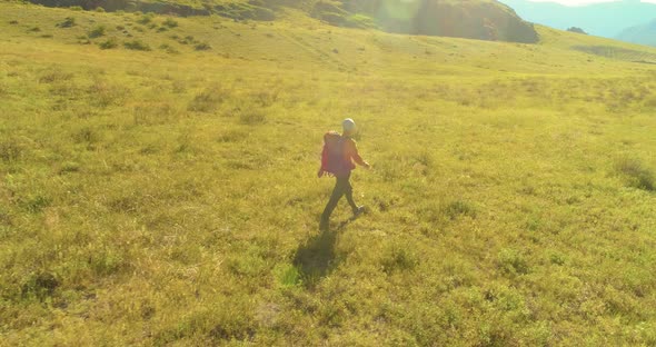Flight Over Backpack Hiking Tourist Walking Across Green Mountain Field. Huge Rural Valley at Summer alt