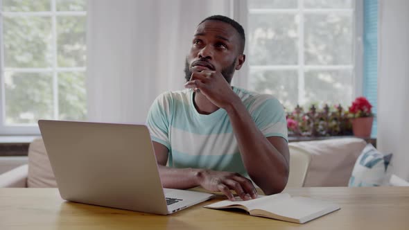 Pensive AfricanAmerican Ethnicity Freelancer Working at Home Using Laptop and Writing Notes alt