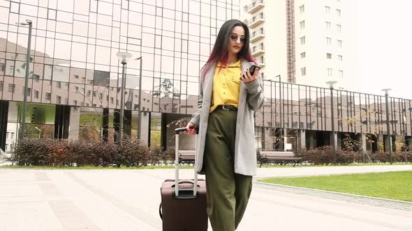 Successful Woman suitcase walks through Parking taxi writes message on phone alt