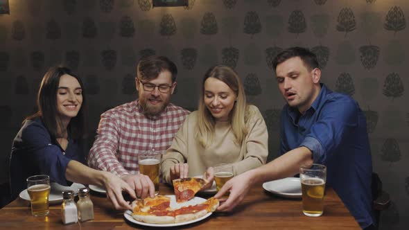 Happy People in Pub Sit at the Table and Take Their Pieces of Pizza Talking with Each Other