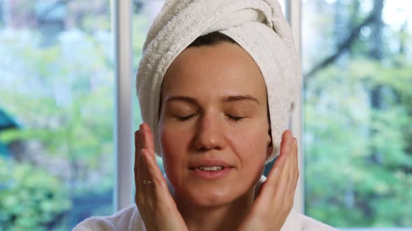 Young Beautiful Woman With a Towel Turban on Her Head Massages Her Face With Her Hands