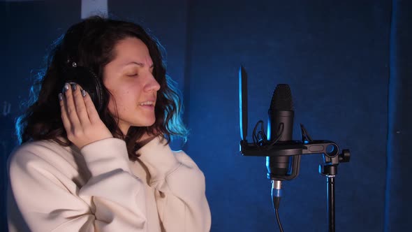 A Young Girl Wearing Headphones Singing in Front of a Studio Microphone While Actively Dancing