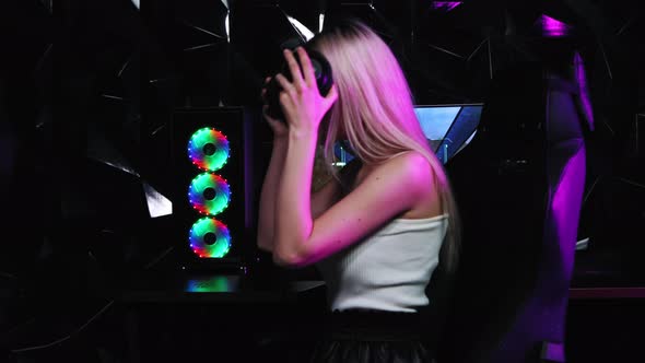 Blonde and Pretty Gamer Girl Puts on Big Headphones and Looking in the Camera alt