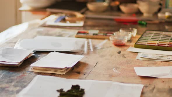 Close up of an artist/painters Messy desk covered in watercolor paints and paintbrushes and other to alt