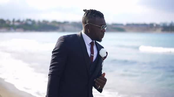 Portrait of Sad African American Groom in Elegant Suit Walking on Mediterranean Sea Beach in Slow alt