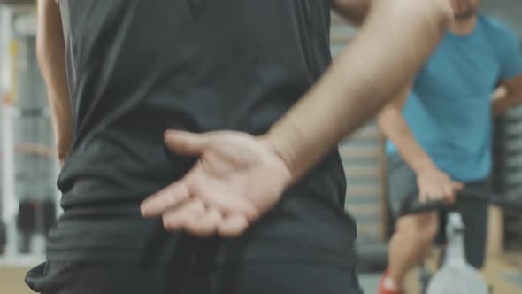 Unrecognizable Sportsman Riding Exercise Bike with One Hand Behind Back. Back View of Sportive alt