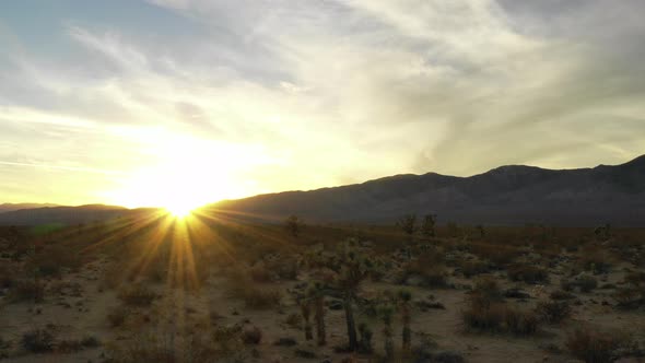 Golden sunrise shining behind silhouette mountains in Mojave Desert, Aerial Pan alt