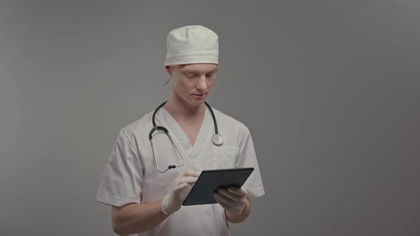Young Doctor In Medical Gown And Gloves He Holds Tablet alt