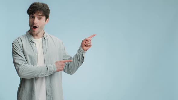 Young Emotional Man Looking Aside and Seeing Surprising Advertisement Pointing Aside at Empty Space alt