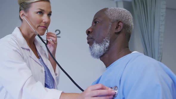 Caucasian female doctor examining african american senior male patient with stethoscope at hospital alt