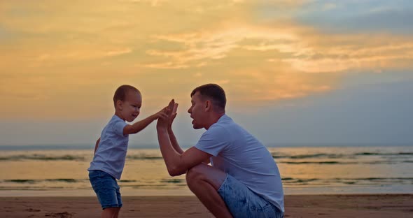 Happy Kid with His Dad is Playing on the Seashore Clapping Their Hands