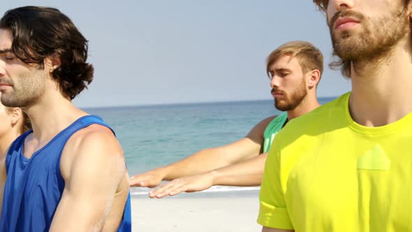 Fit man and woman performing yoga at beach alt