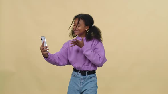 Cheerful African Female Dances to the Music on a Yellow Background and Takes a Selfie Video on alt