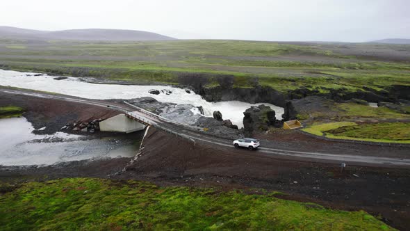 Aerial of a Car Driving on a Little Bridge Across the River Cascades in Iceland alt