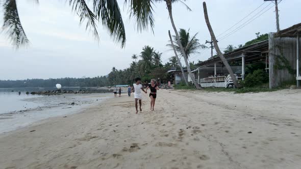 Happy Interracial Couple Running Holding Hands at a Tropical Island Beach at Sunset Aerial Front alt