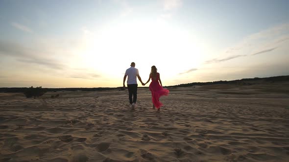 Camera Following to Young Pair Holding Hands and Walking Through Desert alt