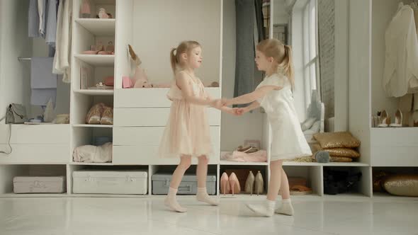 Dancing Little Girls Enjoy New Dress in Clothing Room on Backdrop of Wardrobe with Clothes