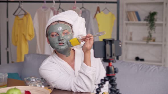 A Girl With a White Towel Put on Her Face a Green Mask During Blogging alt