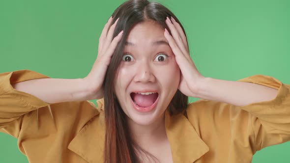 The Shocked Asian Woman Grabbing Her Head While Saying Wow On Green Screen Background In The Studio alt
