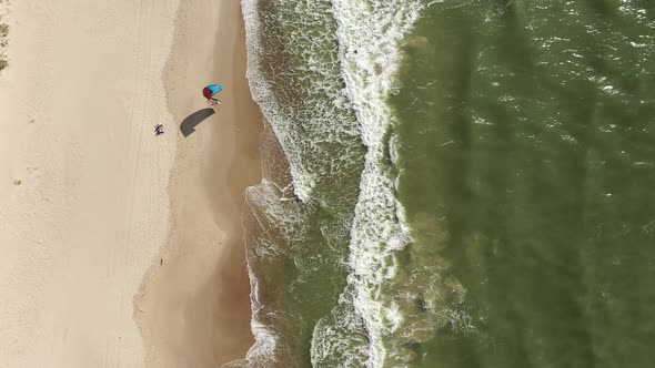AERIAL: Top View Shot of Surfer Trying to Rise Wind Kite while Standing in Sea Water near Beach alt