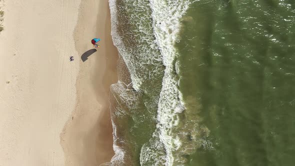 AERIAL: Top View Shot of Surfer Trying to Rise Wind Kite while Standing in Sea Water near Beach