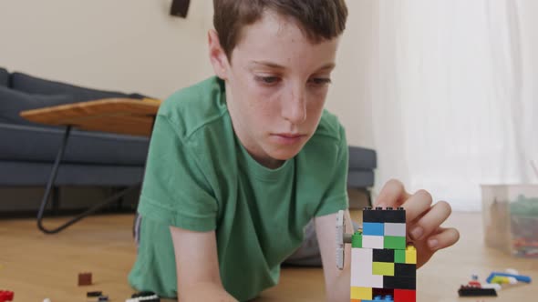 Young boy playing and constructing with toy bricks on the living room floor alt