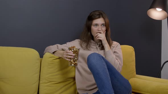 Attractive Longhaired Girl Sitting on Sofa with Popcorn Watching Movie on TV