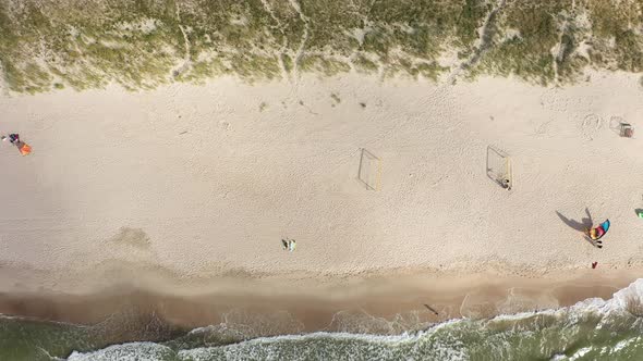 AERIAL: Top View of Long Sandy Beach with Wind Surfers Resting on Shore and Kites Placed on Ground alt