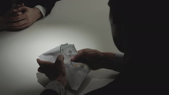 Businessman giving bribe money in the envelope to his partner on the table in dark room