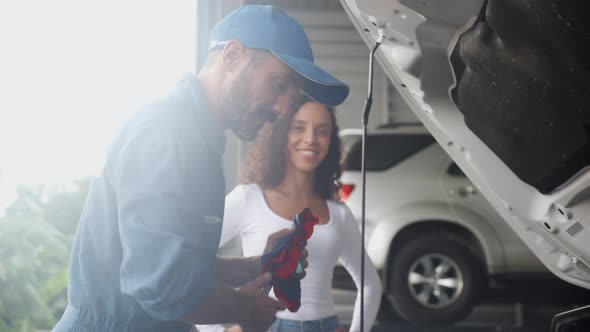 Young man mechanic talking with customer for examining trouble and repairing engine of car. alt
