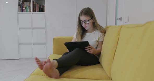 Barefoot Girl in Glasses Sitting on Sofa and Watching Video on Tablet While Resting at Home During alt