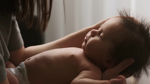 Authentic young mother holds newborn baby in her arms, strokes his hair while he sleeps alt