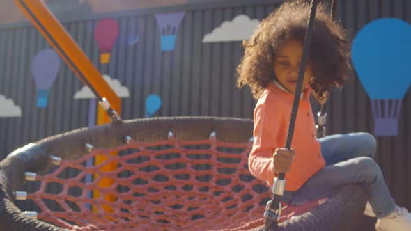 Close Up of African Children Ride on Round Swing with Net in Park alt
