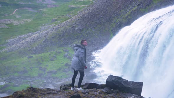Man Watching Fast-flowing Water Of Dynjandi Waterfall In Arnarfjordur In Westfjords of Iceland. alt