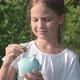 Happy Kid Girl Puts Money Into Piggy Bank on Green Nature Background - VideoHive Item for Sale