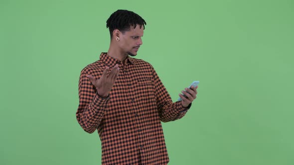 Happy Young Handsome African Man Using Phone and Looking Surprised alt