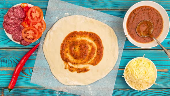 Top view of cooking pizza with ingredients on blue wooden background.