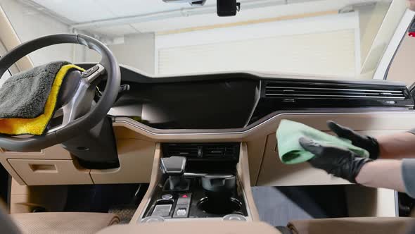Male Worker Cleaning Car Interior with a Cloth Spraying a Detergent on It and Wiping Car's Dashboard alt