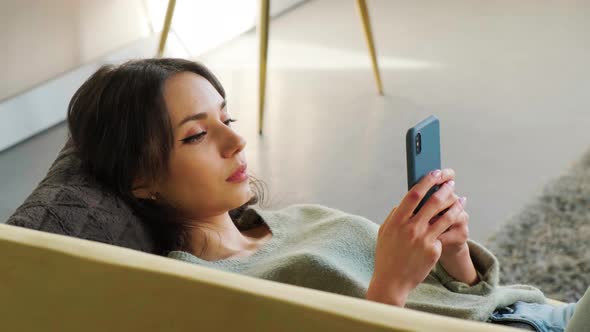 Woman Surf the Internet on Her Mobile While Relaxing on a Sofa in Her Living Room alt
