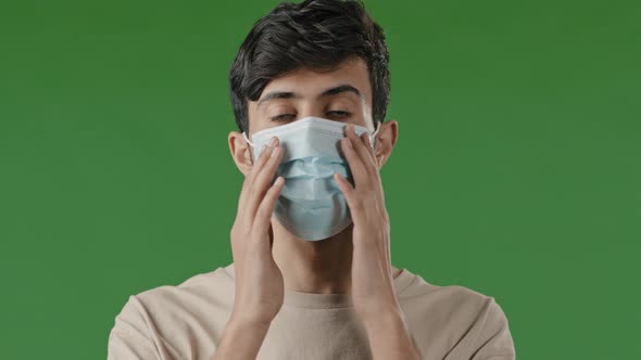 Close Up Serious Young Arab Guy Putting on Medical Mask Standing in Studio on Green Background alt