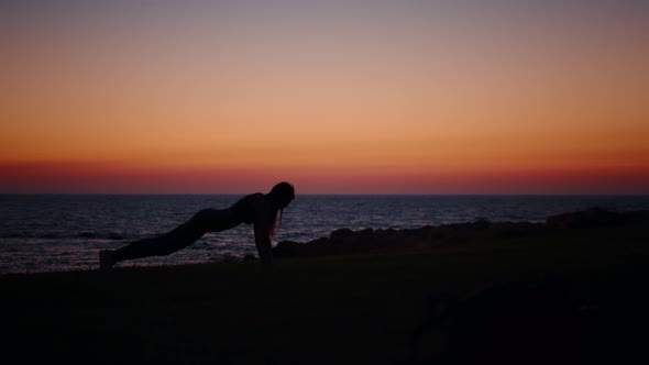 Woman in Silhouette Standing in Plank Position Near Ocean alt
