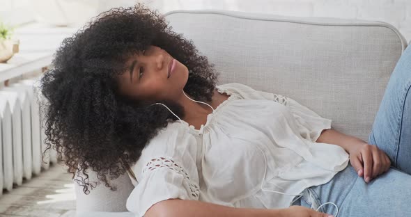 A Relaxed Young Black Smiling Woman Wearing Headphones Resting on a Comfortable Couch