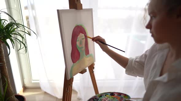 Girl Sits on a Chair Near the Easel and Holds a Palette and a Brush in Her Hands alt