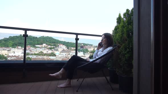 Concentrated Lady in Glasses Talks on Smartphone Sitting on Terrace alt