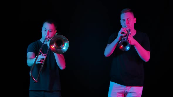 Male Musicians Play the Trombone and Trumpet in the Studio on a Black Background in Neon Light alt