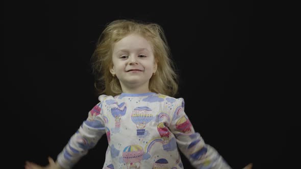 Little Baby Girl in Pajama Is Fooling Around and Make Faces. Black Background alt