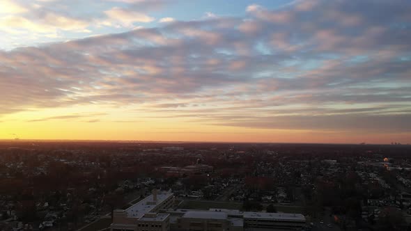 An drone view of a Long Island neighborhood during a golden sunrise with clouds and blue skies. The alt
