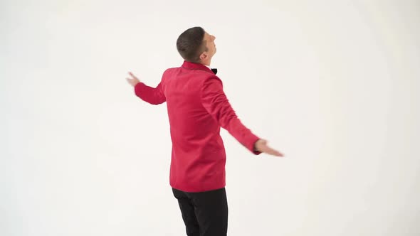 showman in a red jacket with a bow tie is circling around himself with openarmed hands alt
