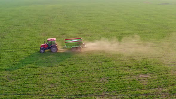A red tractor against a background of a green field sprays mineral fertilizers.